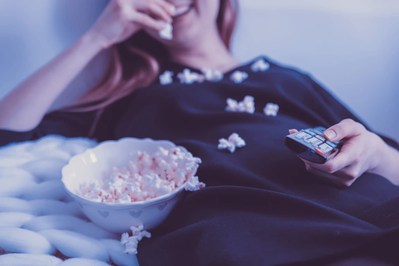 Kvinna som ligger i sängen och äter popcorn framför en film